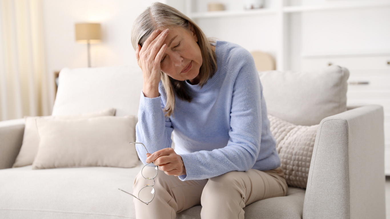 Woman sitting on couch holding glasses and experiencing fatigue or headache at home